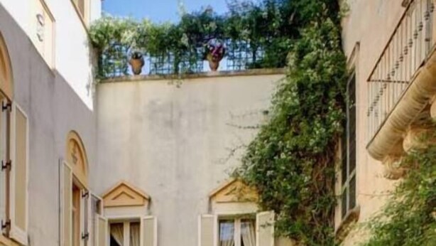 Un patio con un edificio que tiene puertas con arcos, una bicicleta y macetas con plantas.