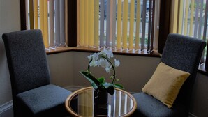 A corner room with two chairs, a small table, and a vase with flowers.