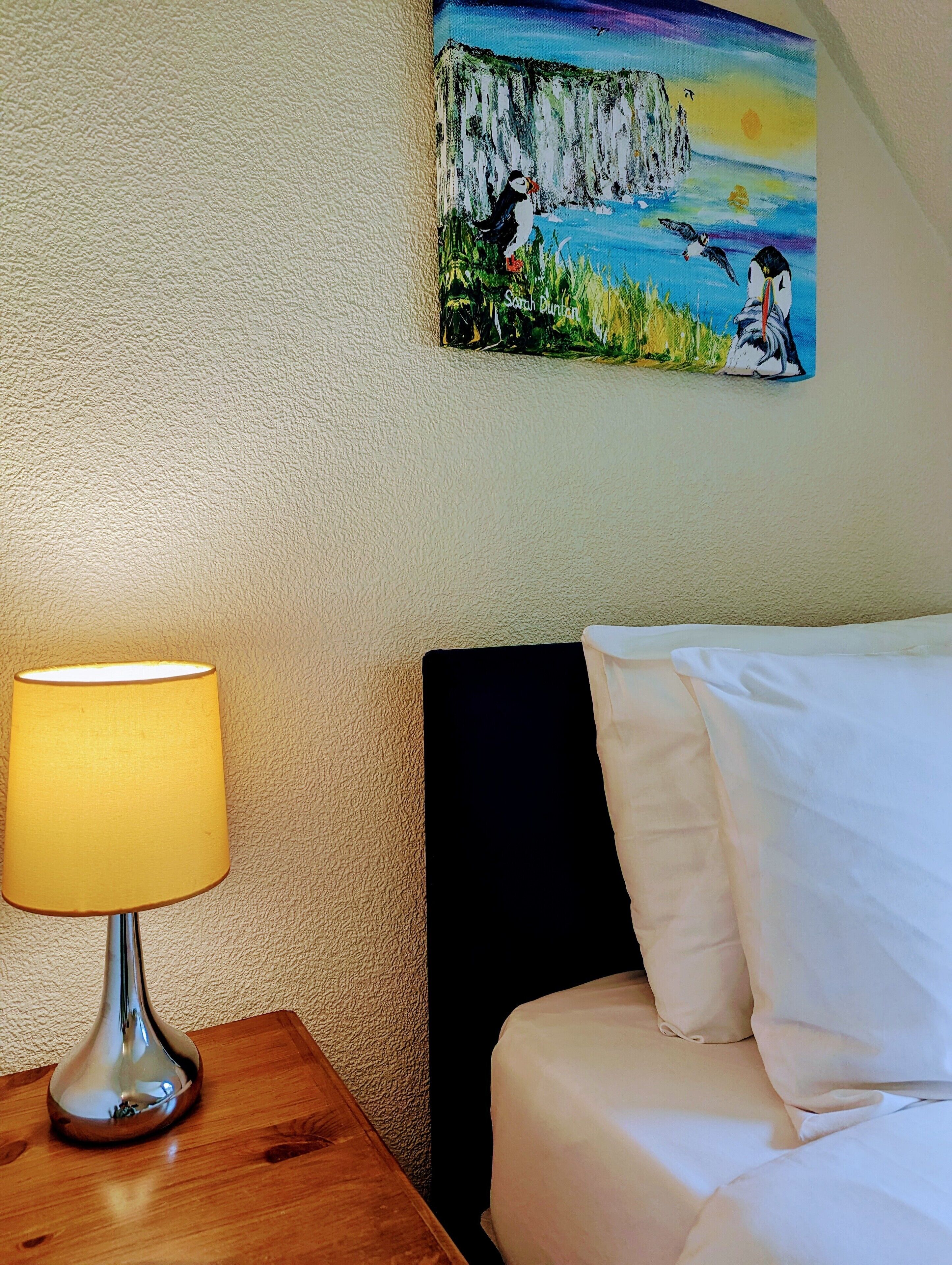 Een hotelkamer met een bed, een nachtkastje met een lamp en een schilderij aan de muur.