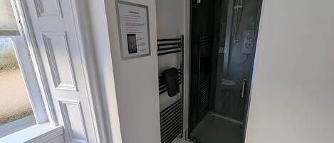 A bathroom with a glass shower door, a towel rack, and a white door with a decorative trim.
