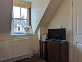 Una habitación con ventana, radiador, televisor, armario y un cubo de basura.