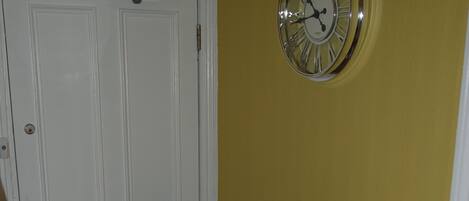 A room with a wooden barrel, a laptop on a small table, a door, and a wall clock.