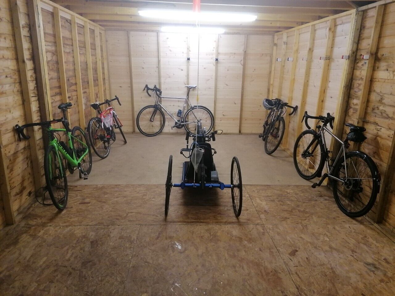 A room with wooden walls and a tiled floor, containing several bicycles and a tricycle.