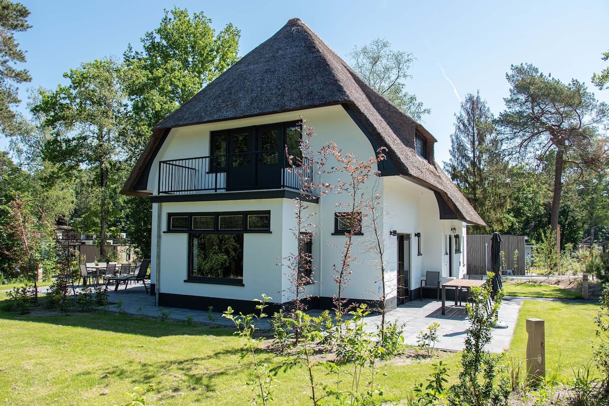Une maison à deux étages avec un toit de chaume, un balcon et un jardin.