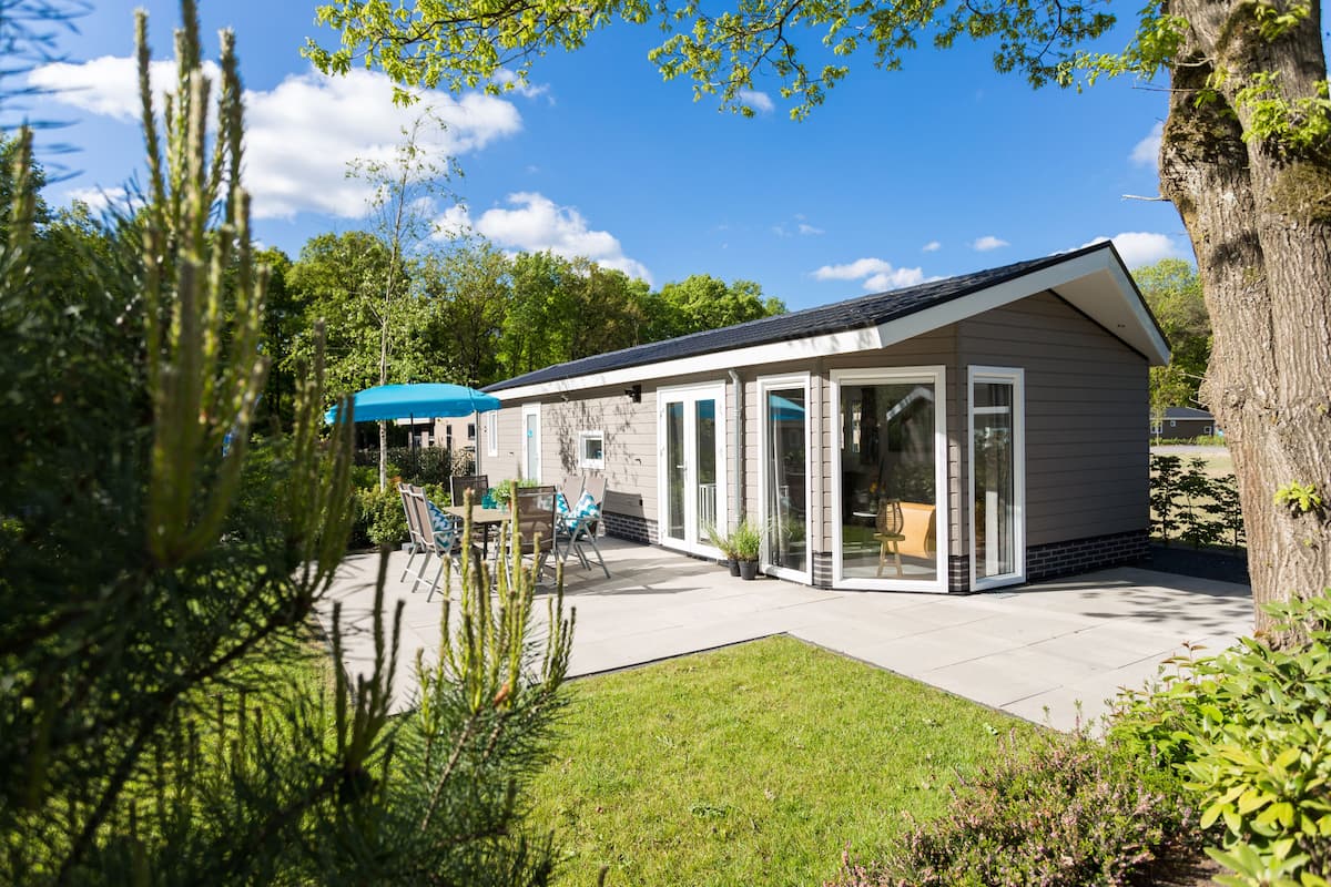 Une maison moderne dotée d’une terrasse, d’un parasol bleu et d’une pelouse bien entretenue.