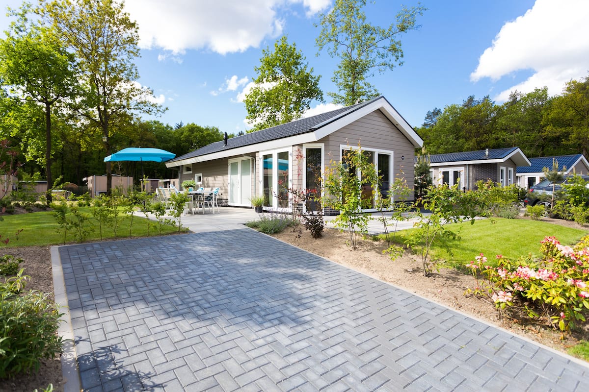 Une maison moderne avec une allée pavée, entourée de jardins et d’arbres bien entretenus.
