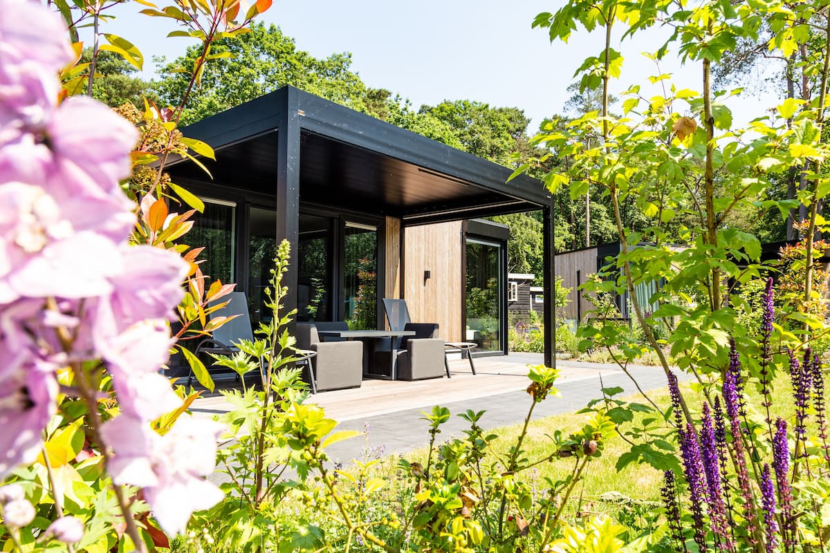 Une terrasse extérieure moderne, avec une table et des chaises en bois, entourée d’une végétation luxuriante et de plantes en fleurs.