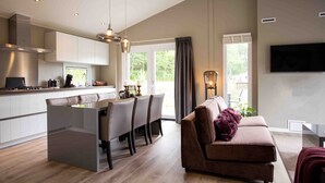 A modern kitchen with a dining area, a sofa, and a TV in a living room.