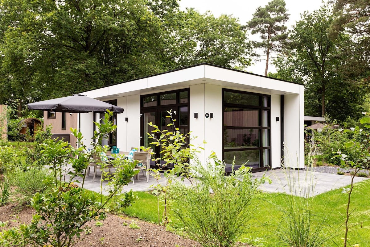 Un bâtiment moderne, de plain-pied, doté d’un toit plat, de grandes fenêtres et d’un patio aménagé avec des sièges extérieurs.