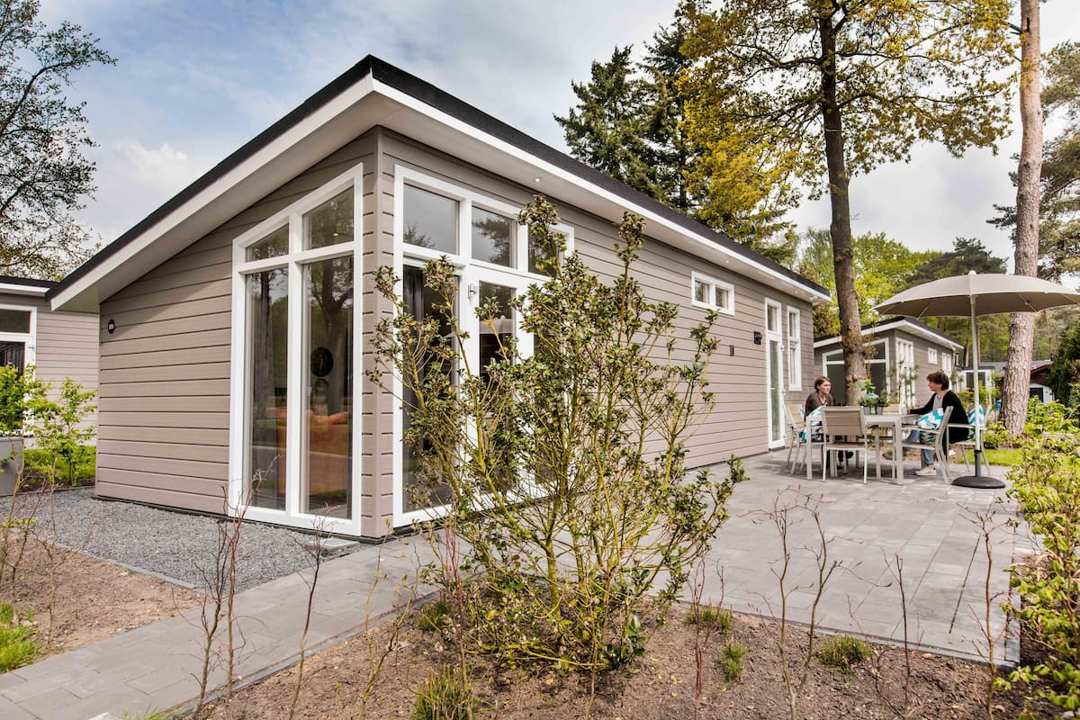 Une maison moderne dotée d’un patio, de grandes fenêtres et d’une table à manger avec des chaises.