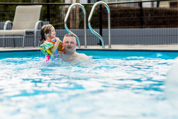 A swimming pool with clear water, a child and an adult in the water, and a poolside area with lounge chairs and a fence. - TopParken Recreatiepark Beekbergen (Beekbergen)