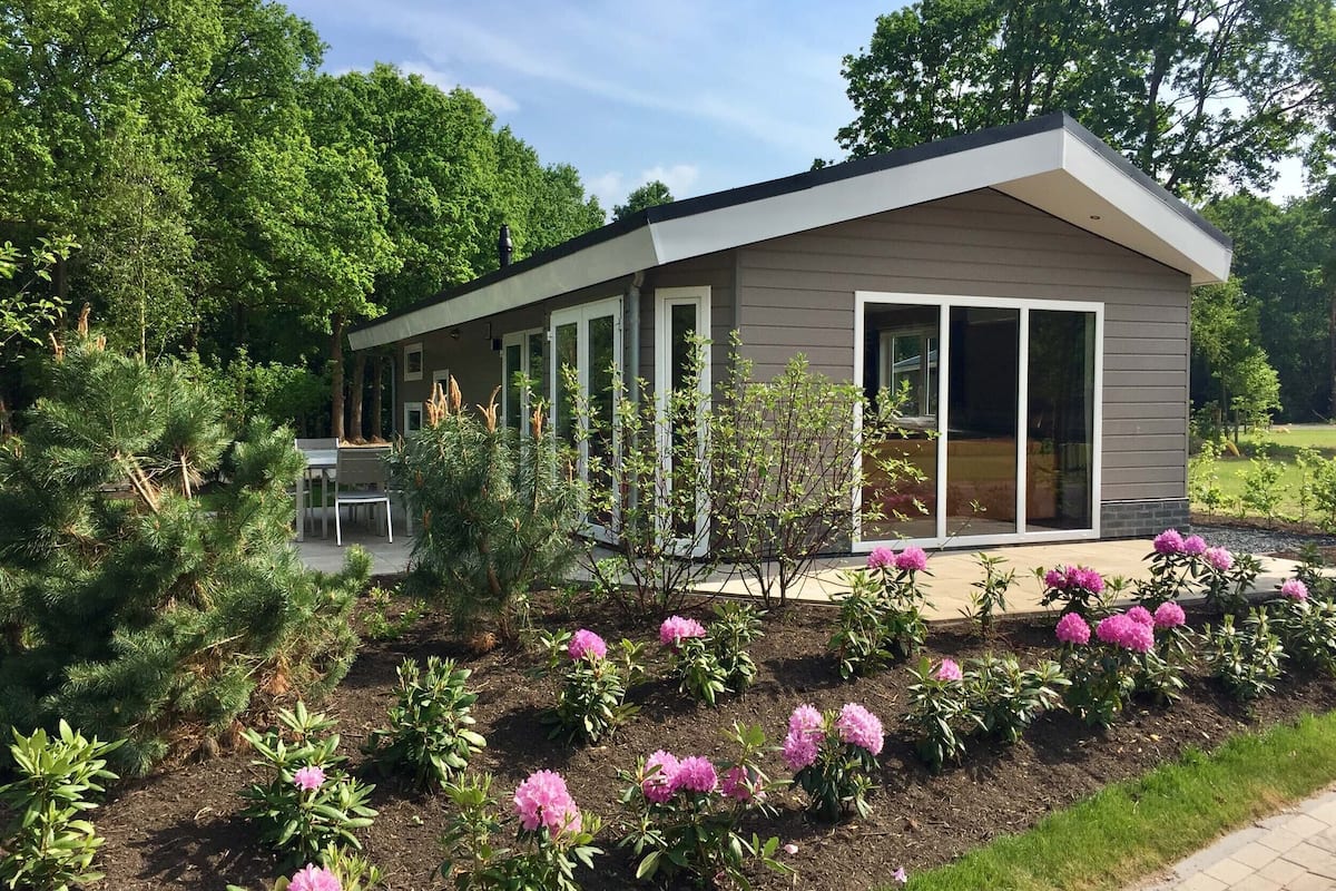 Une maison moderne dotée d’un patio, entourée d’un jardin agrémenté de fleurs roses et de divers arbustes.