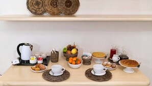 Un desayuno con cestas de mimbre, una tetera, tazas, un frutero, pasteles y un pastel en una mesa de madera.