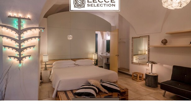 Una habitación de hotel con una cama grande, una mesita de noche, un espejo, un sofá y una lámpara de pared decorativa.