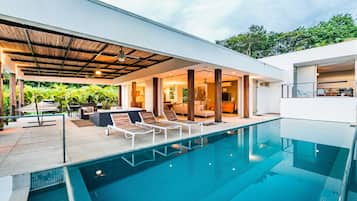 A modern house with a swimming pool, outdoor seating, and a covered patio.