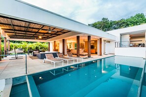 Una casa moderna con piscina, mobiliario de exterior y terraza cubierta.