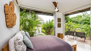 A bedroom with a large bed, a wooden headboard, and a view of lush greenery outside.