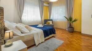 A bedroom with a bed, bedside lamp, curtains, a potted plant, and a wooden floor. - Apartment Cabo (Split)