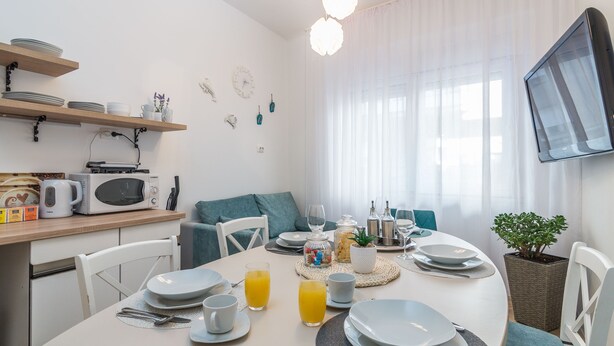 A modern dining area with a round table set for breakfast, white plates, and glasses of orange juice. - Apartment Cabo (Split)