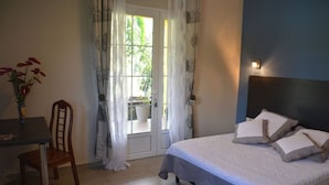 A bedroom with a bed, a chair, a table, and a window with curtains. - Le Guetali (Salazie)