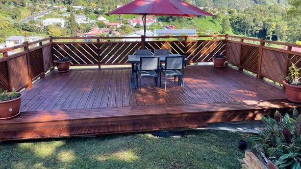 A wooden deck with a table and chairs, surrounded by a wooden fence, overlooking a mountainous landscape. - Le Guetali (Salazie)