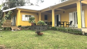 A yellow building with a covered patio area, outdoor seating, and potted plants. - Le Guetali (Salazie)