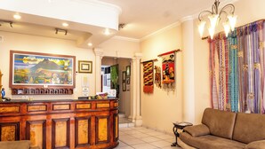A lobby with a reception desk, a sofa, and a chandelier. - Hotel Indio Inn (Otavalo)