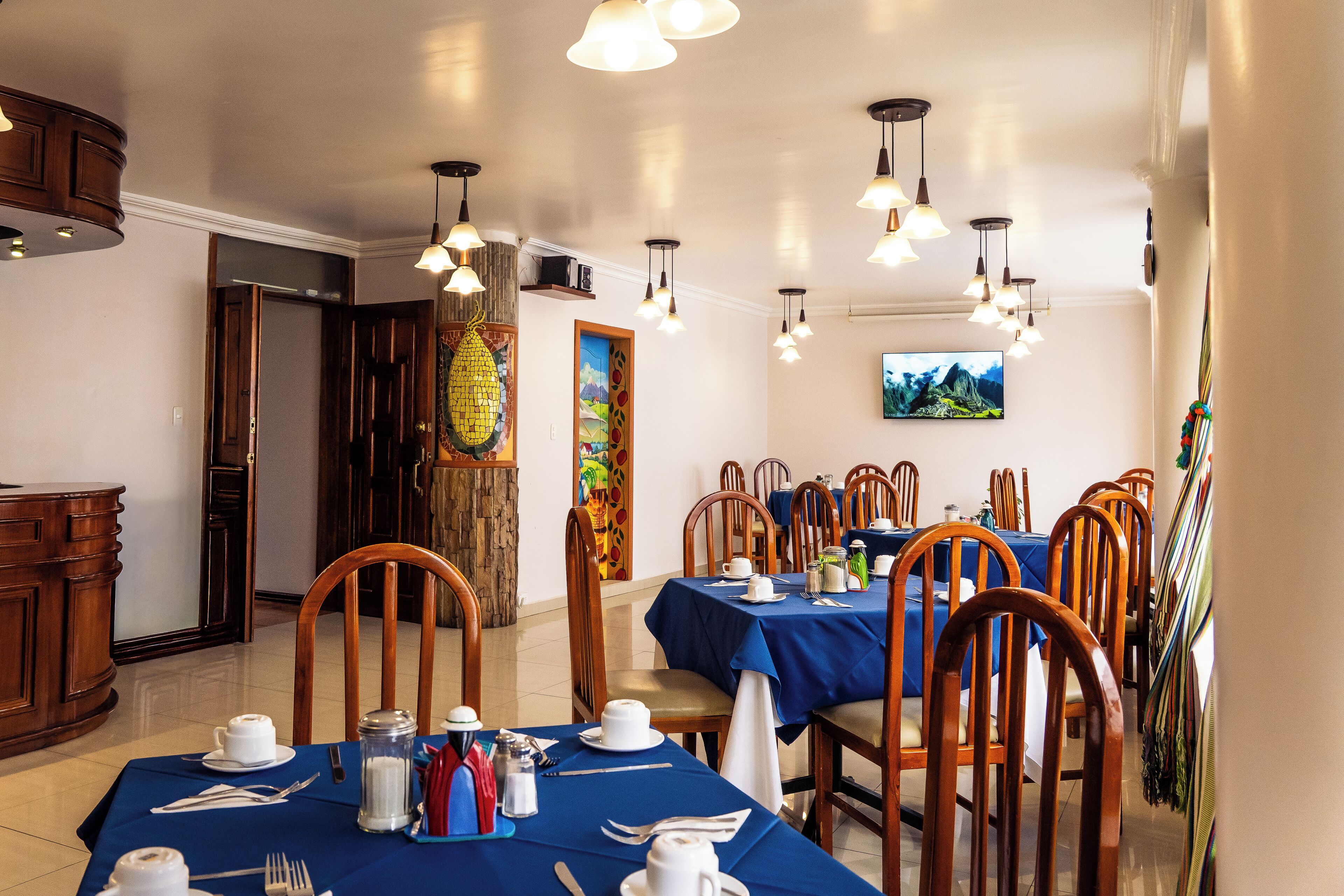 A dining area with multiple tables set for meals, wooden chairs, and pendant lighting.