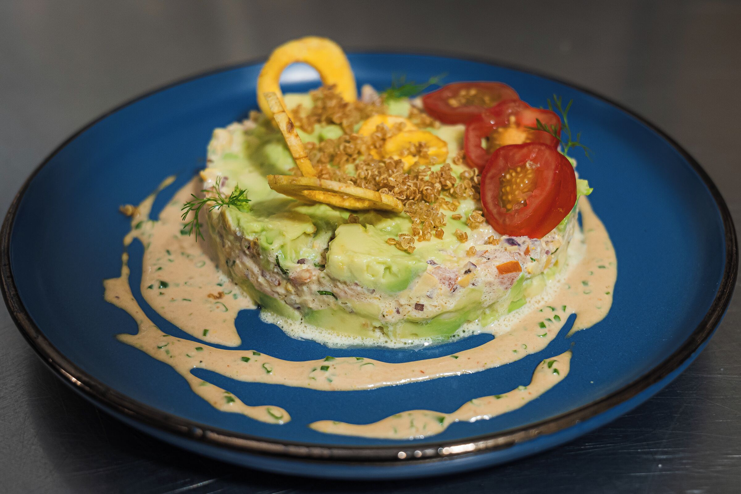 A dish with avocado, tomatoes, and a creamy sauce on a blue plate.