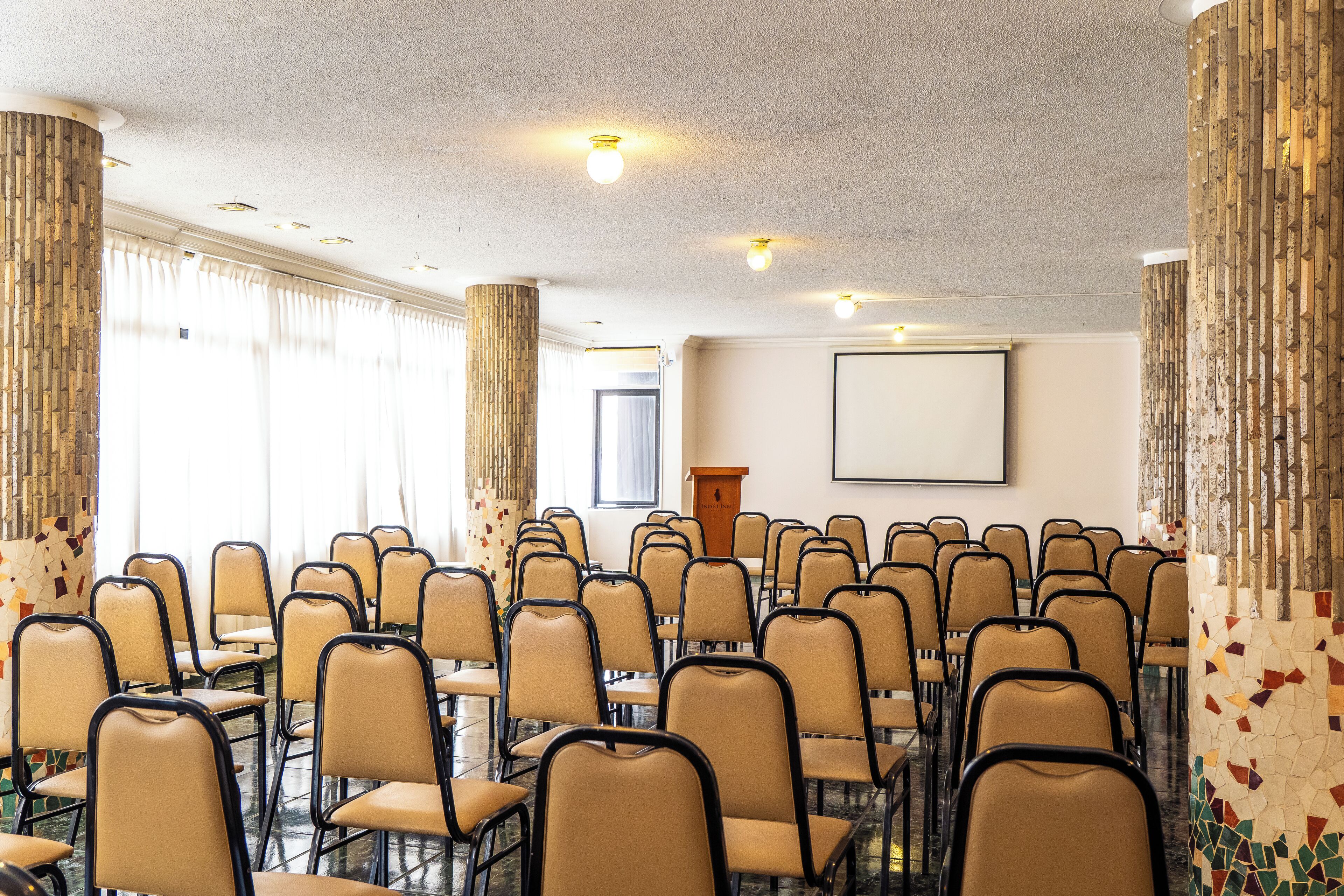 A conference room with rows of chairs, a podium, and a projector screen.