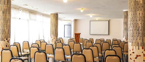 Un salón de conferencias con filas de sillas, un atril y una pantalla para proyector.
