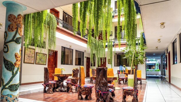 A spacious lobby with wooden chairs and tables, hanging plants, and a tiled floor. - Hotel Indio Inn (Otavalo)