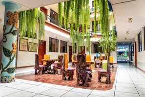 A spacious lobby with wooden chairs and tables, hanging plants, and a tiled floor. - Hotel Indio Inn (Otavalo)