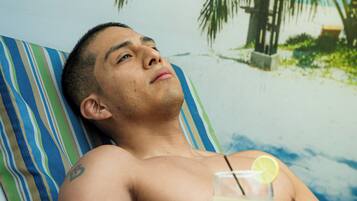 A person lying on a striped beach-themed lounge chair, holding a cocktail with a lemon slice, with a palm tree and ocean in the background.