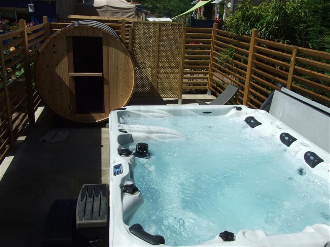 A hot tub with a wooden barrel and a wooden fence in a garden setting.