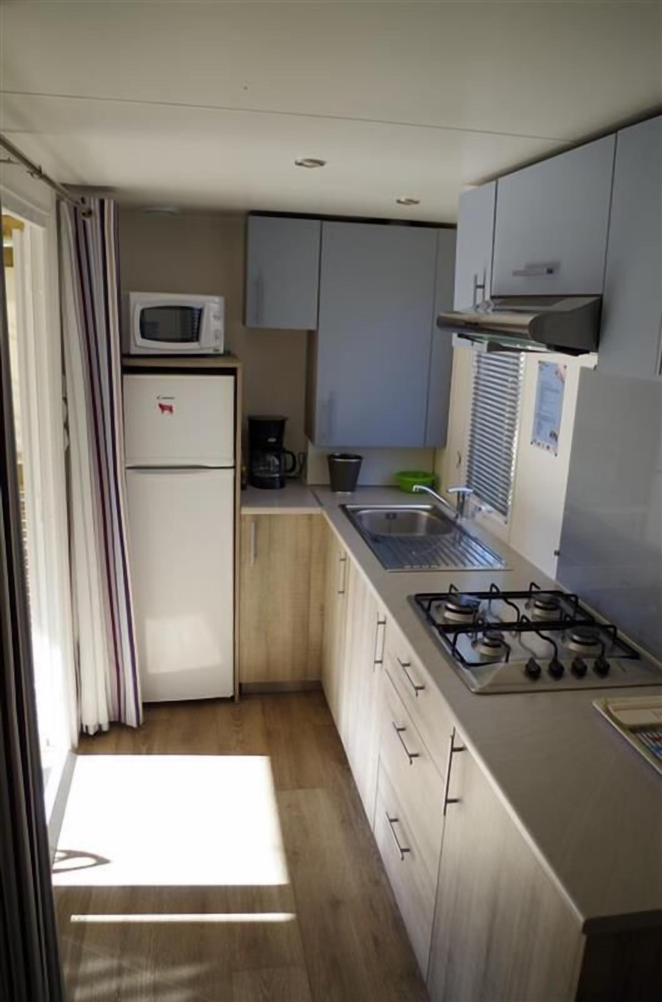 Eine kompakte Küche mit Kühlschrank, Mikrowelle, Gaskochfeld, Spüle und Schränken.
