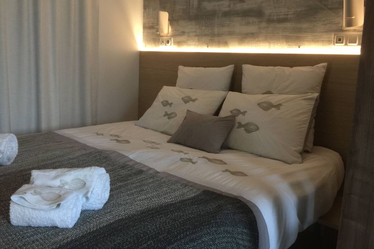 Una habitación de hotel con una cama bien hecha, un cabecero con iluminación integrada y una ventana con cortinas.
