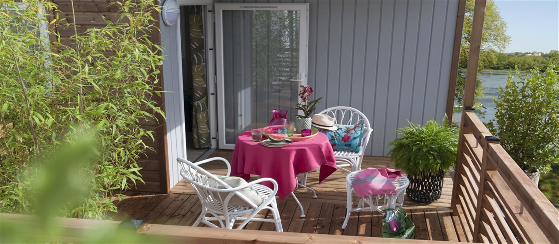 A wooden deck with a table and chairs, a potted plant, and a view of a body of water.