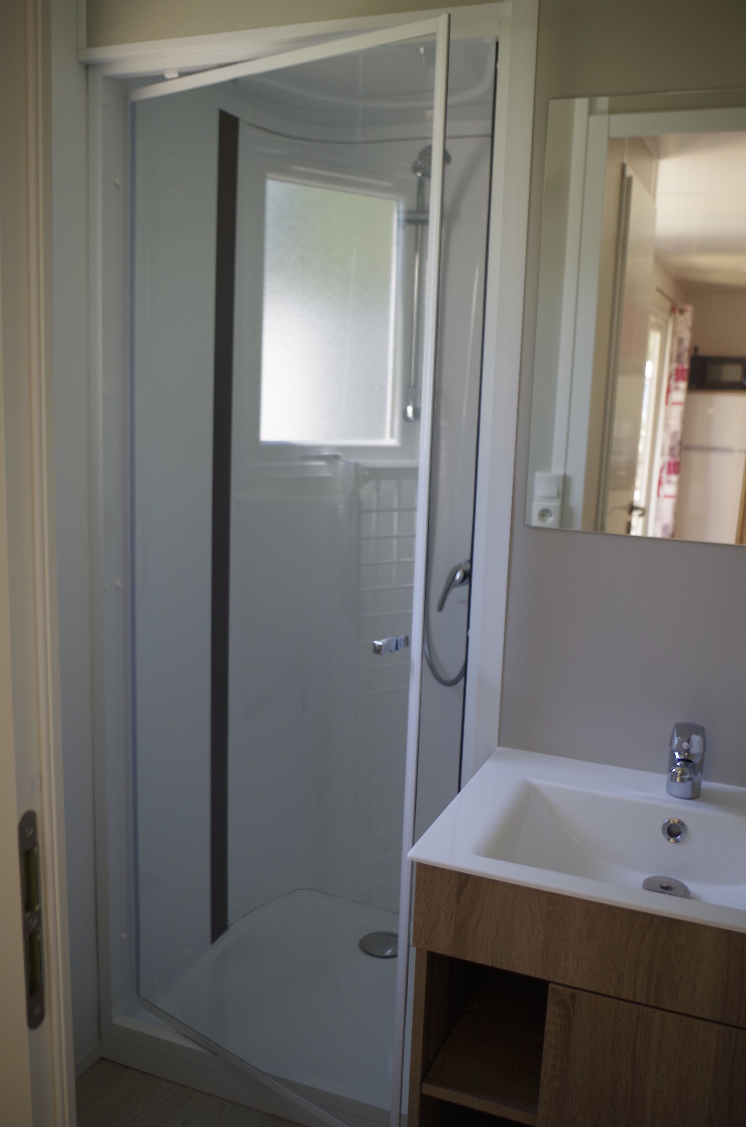 Un baño con ducha de vidrio, un lavabo blanco y un mueble de tocador de madera.