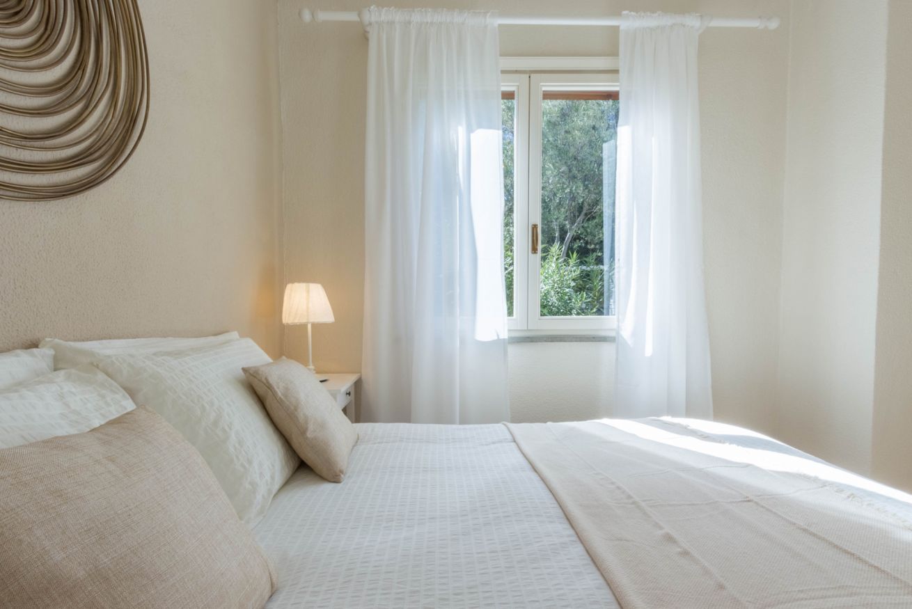 A bedroom with a bed, a nightstand, a lamp, and a window with curtains.