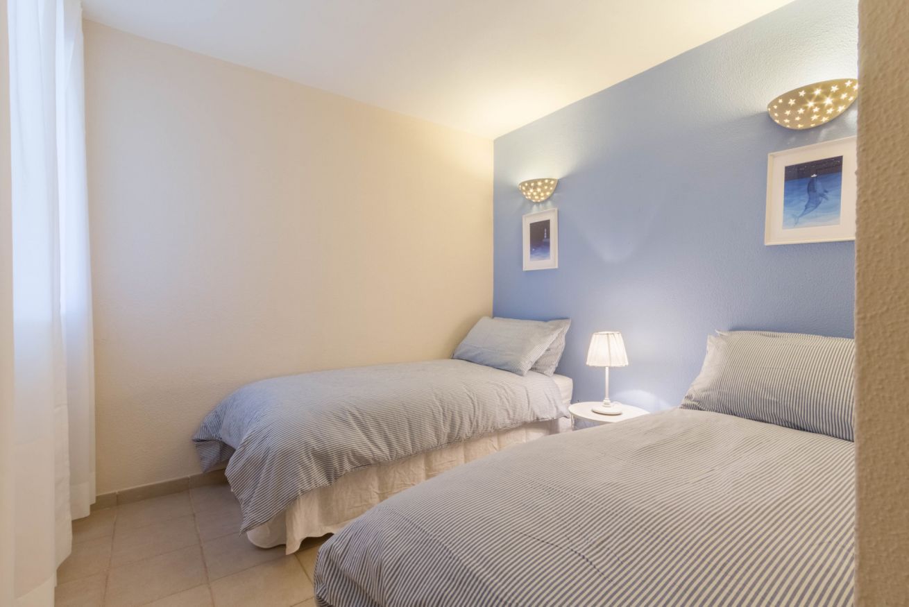 A bedroom with two beds, a nightstand with a lamp, and a wall-mounted light fixture.