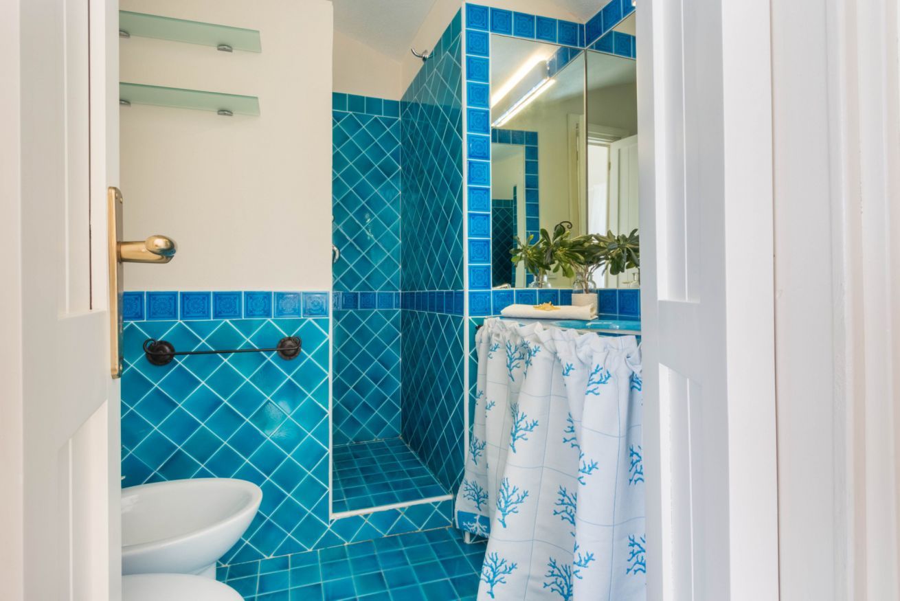 A bathroom with blue tiles, a white sink, a glass shower enclosure, and a mirror.