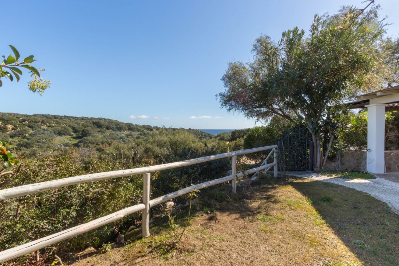 A view of a rural landscape with a wooden fence, a tree, and a building in the background.