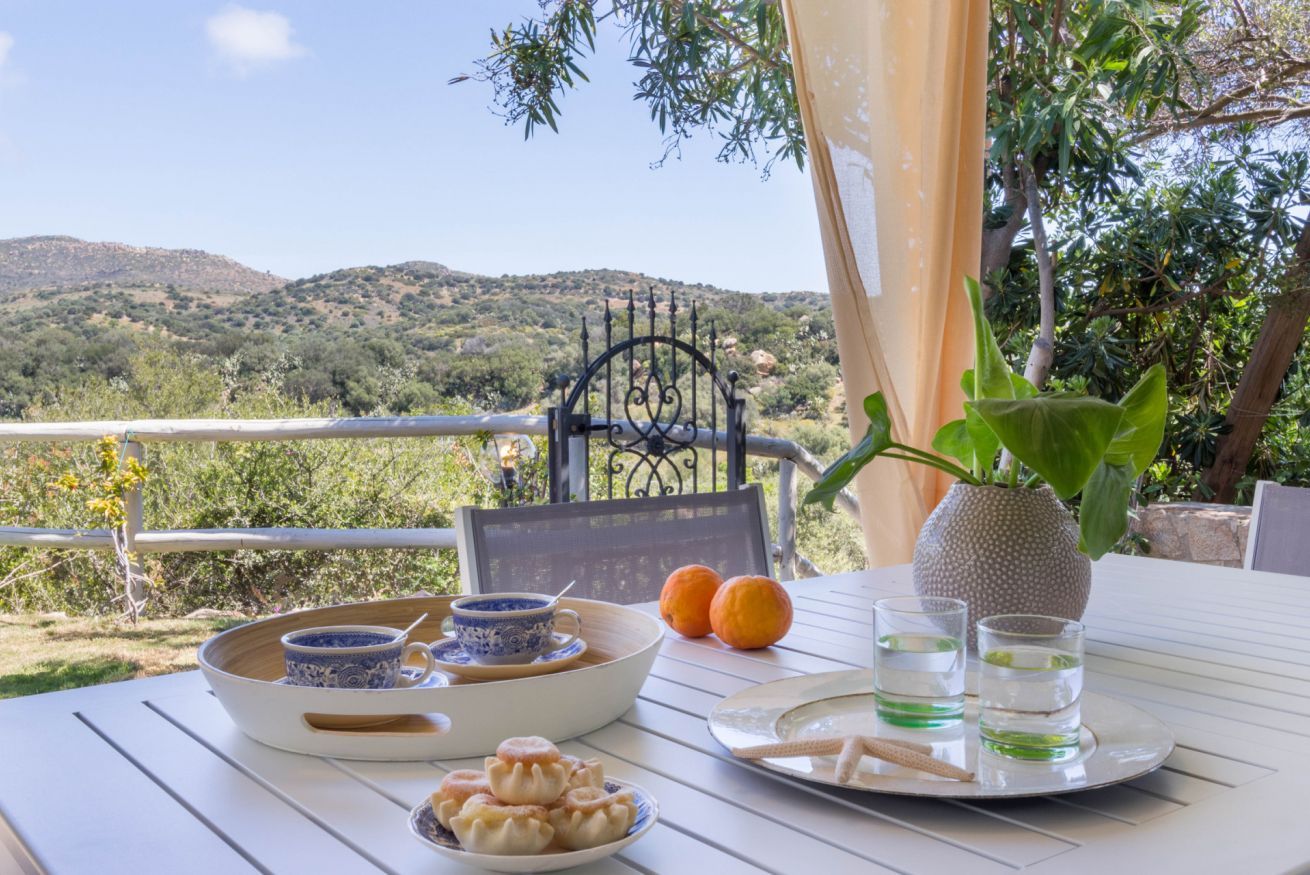 Une table dressée avec un saladier rempli de pâtisseries, une assiette avec deux oranges, un vase avec une plante et deux verres d’eau.