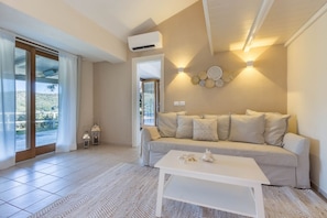 A living room with a beige sofa, a white coffee table, and a view through a glass door.