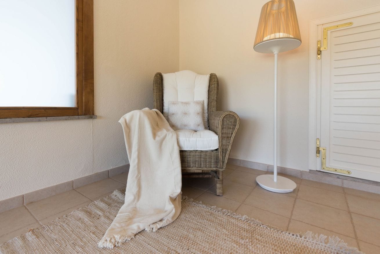 Ein Zimmer mit einem Korbstuhl, einer weißen Stehlampe und einer weißen Tür.