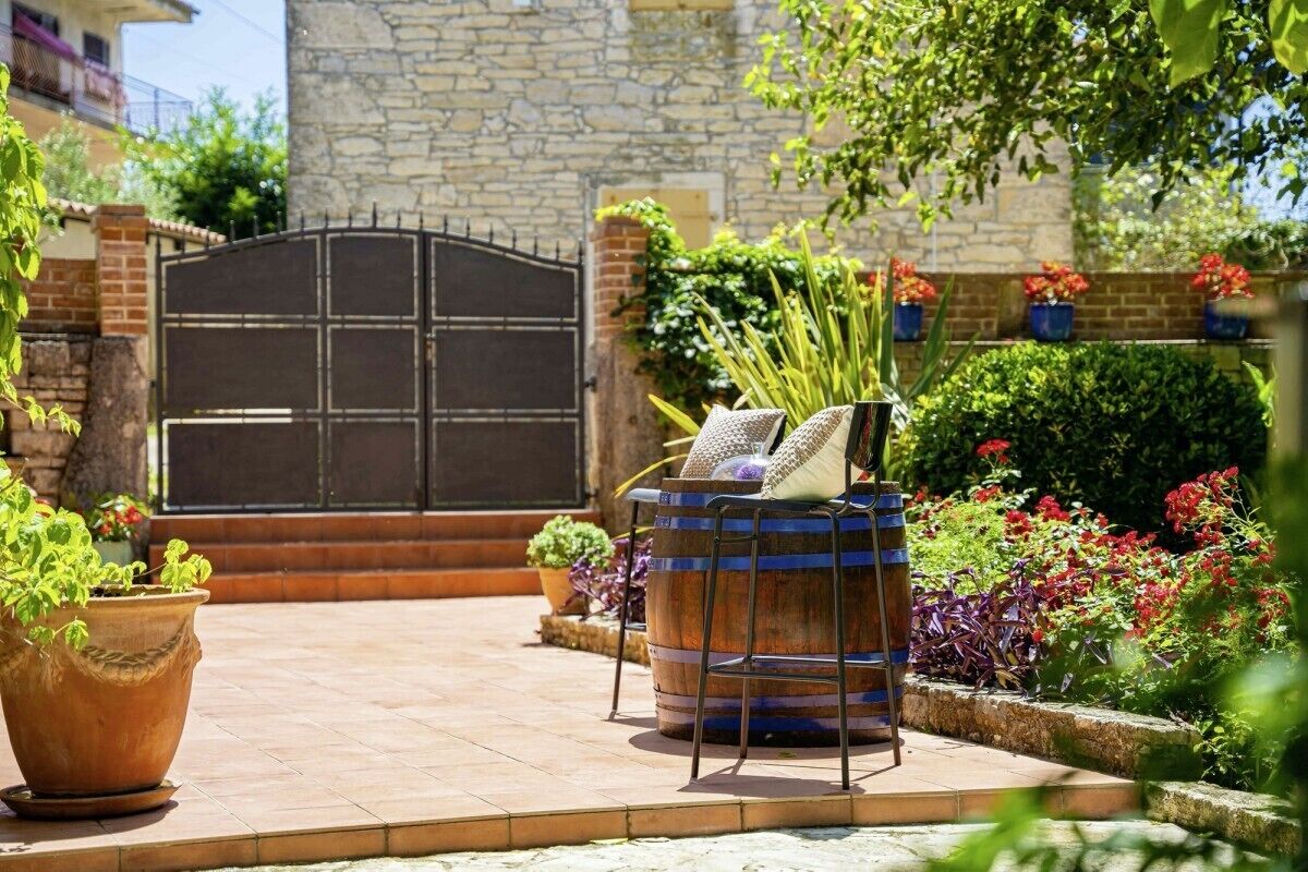 A courtyard with a stone wall, a metal gate, and potted plants.
