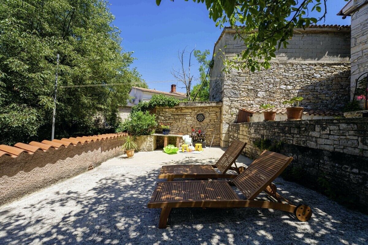 A courtyard with two wooden lounge chairs, a stone wall, and a small outdoor kitchen area.