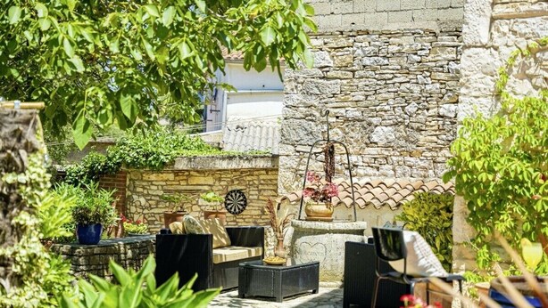 Un muro de piedra con un dardo, asientos exteriores con muebles de mimbre y plantas en macetas.