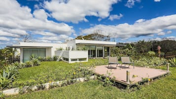 A modern house with a patio, surrounded by lush greenery and a clear blue sky.